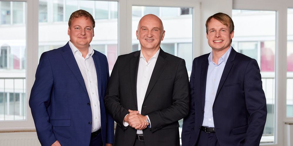 Gruppenbild von drei Männern in Anzügen, die in die Kamera lächeln