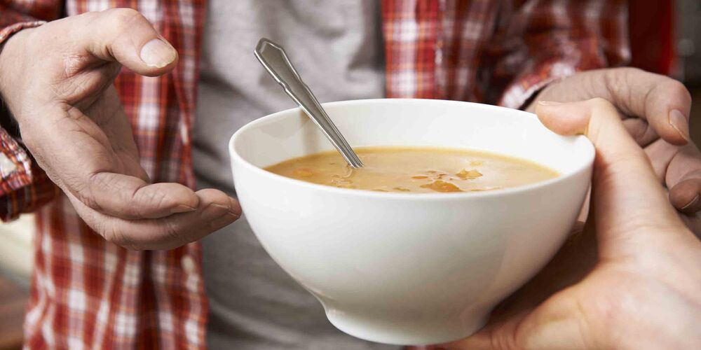 Eine Hand reicht einem Mann eine Schüssel mit Suppe. 