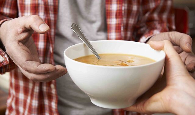 Eine Hand reicht einem Mann eine Schüssel mit Suppe. 