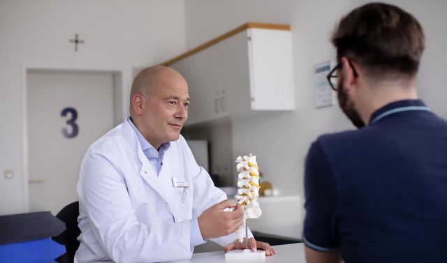 Ein Facharzt für Neurochirurgie erklärt einem Patienten ein Behandlungsverfahren der Wirbelsäule.