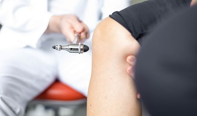 Ein Arzt klopft mit einem kleinen Hammer gegen das Knie eines Patienten.