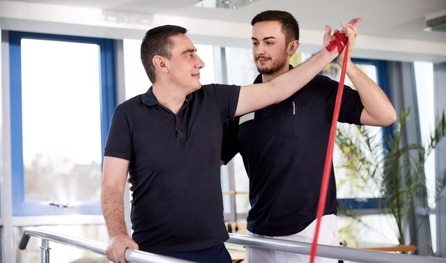 Ein Ergotherapeut führt gemeinsam mit einem Patienten bei der Ergotherapie Übungen für den Arm durch.