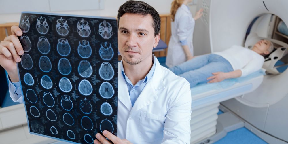 Ein Arzt für Neurologie prüft den CT-Scan einer Patientin, die man im Hintergrund sieht.