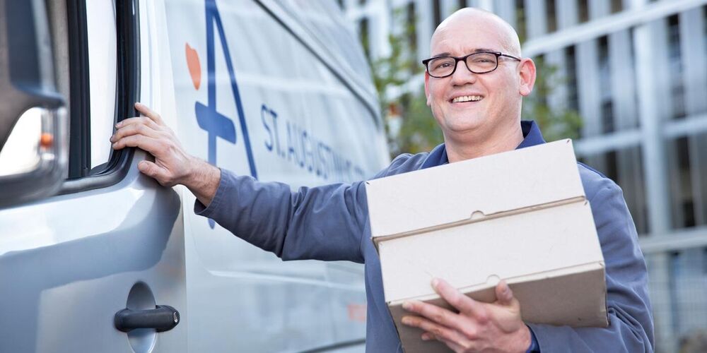 Ein Mann hält zwei Pakete in einer Hand und hat die andere an einen Transporter mit einem Augustinus Logo. 