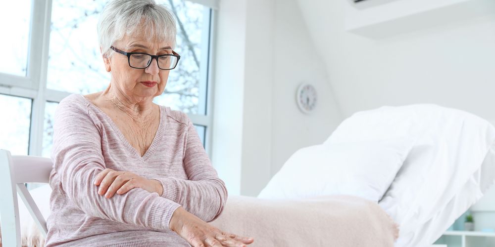 Eine Frau, die ihren Arm umfasst, symbolisiert Lähmungserscheinungen als Symptom der ALS-Krankheit.