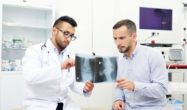 Ein Arzt zeigt einem Patienten mögliche Behandlungsmethoden beim Bänderriss. 