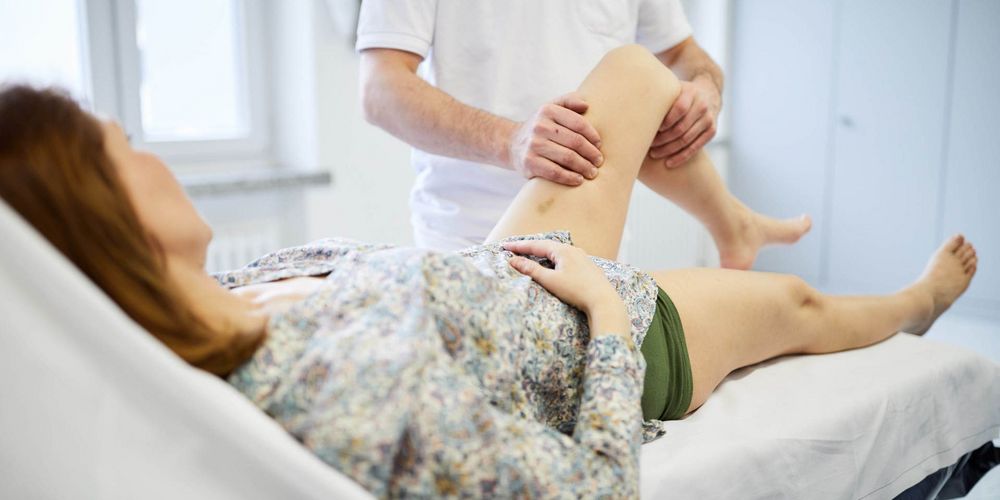Ein Mitarbeiter der Abteilung für multimodale Schmerztherapie untersucht das Knie einer Patientin auf Schmerzen.