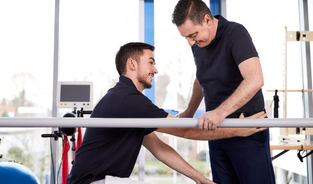 Ein Therapeut hilft einem Mann während der Reha beim Wiedererlangen der Mobilität