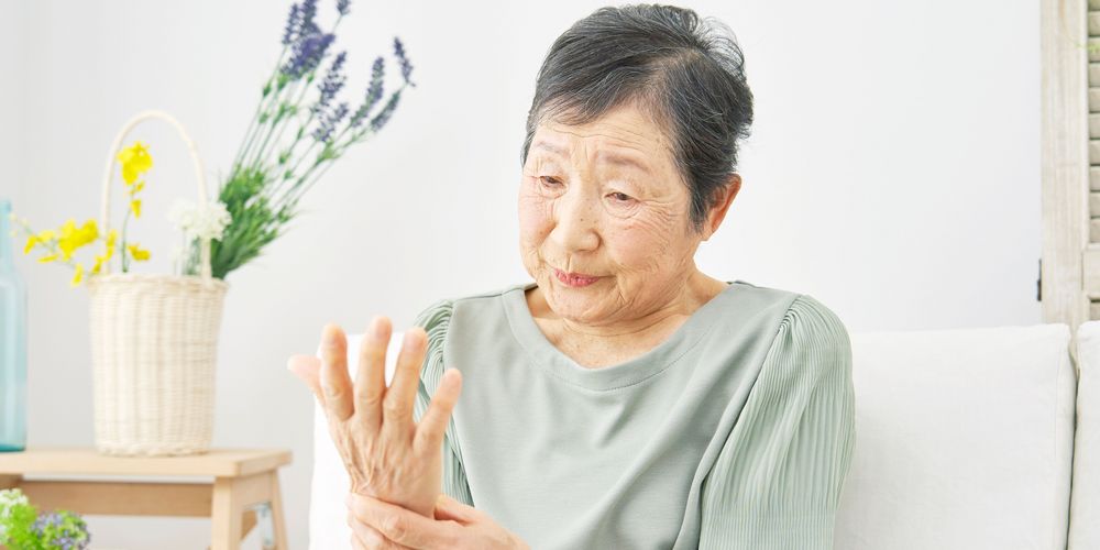 Lähmungserscheinungen an Arm und Händen als Symptom des Guillain-Barré-Syndroms Eine Frau, die ihren Arm umfasst, symbolisiert Lähmungserscheinungen als Symptom des Guillain-Barré-Syndroms.