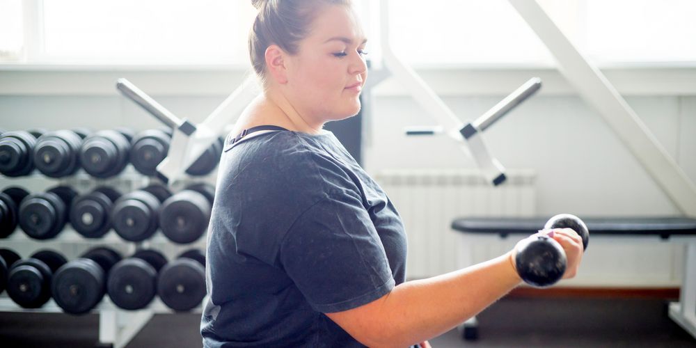 Eine übergewichtige Frau macht Krafttraining mit Hanteln als Teil ihrer Bewegungstherapie bei Adipositas.