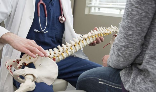 Ein Facharzt für Chirurgie zeigt einer Patientin eine Behandlungsmethode an der Wirbelsäule.
