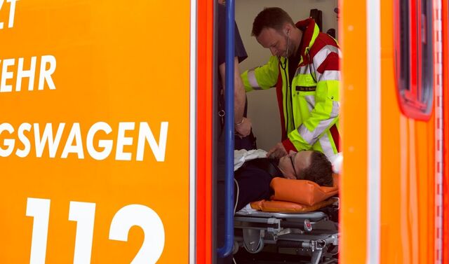 Blick in einen Rettungswagen, der die Tür geöffnet hat. In diesem steht ein Rettungssanitäter und behandelt einen Patienten.