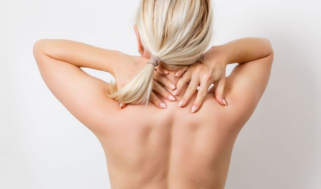 Eine Frau zeigt ihren Rücken mit Lordose, der physiologischen Krümmung der Wirbelsäule. 