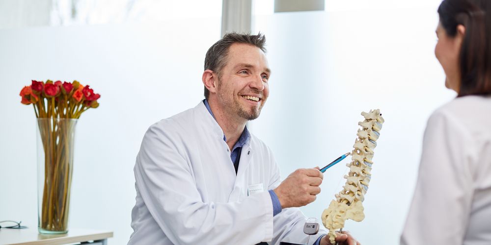 Ein Arzt berät eine Patientin zur Therapie der Schmerzen durch ihre ausgeprägte Lordose.