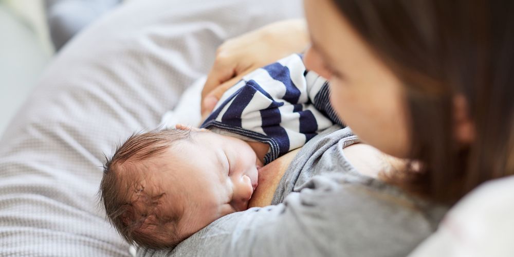 Eine Mutter hält ihr Neugeborenes im Wochenbett liebevoll im Arm.