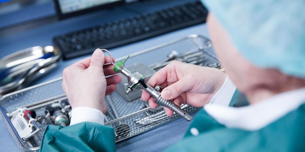 Eine Person in OP Kleidung hält medizinisches Besteck in der Hand und weiteres liegt vor ihr. 