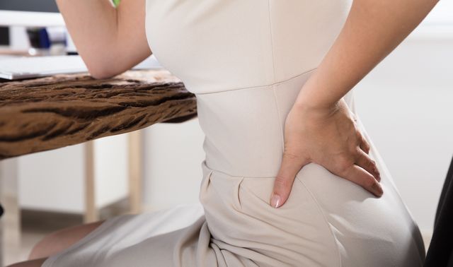 Eine Frau hat Rückenschmerzen als Symptom einer krankhaften Lordose (Hyperlordose).