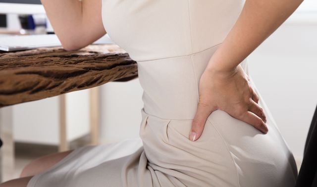 Eine Frau hat Rückenschmerzen als Symptom einer krankhaften Lordose (Hyperlordose).