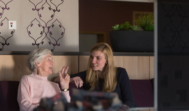Das Bild zeigt eine ältere und jüngere Frau, sie sich im Gemeinschaftsraum unterhalten.