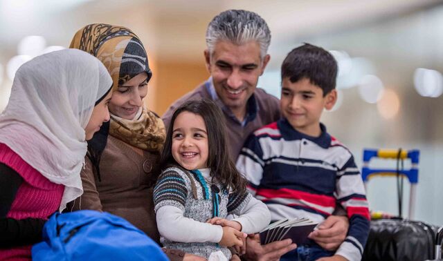 Eine Familie mit Flüchtlingshintergrund sitzt lächelnd beisammen. Sie besteht neben den Eltern aus drei Kindern.