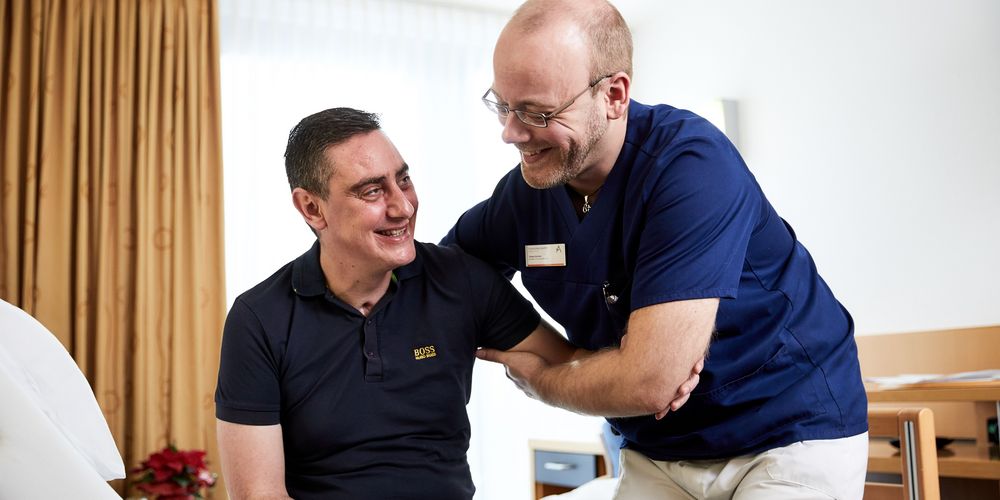 Ein Krankenpfleger betreut einen Patienten in der Allgemeinchirurgie nach einer hernienchirurgischen Operation.