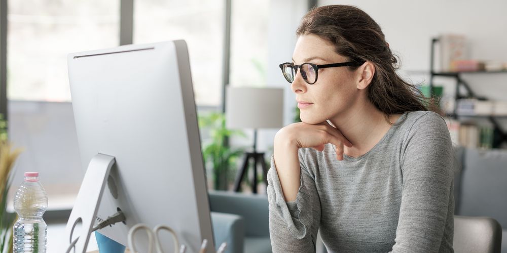 Viel sitzen und wenig Bewegung sind Ursachen für Rückenschmerzen Eine sitzende Frau vorm Computer steht für wenig Bewegung als Ursache für Rückenschmerzen.
