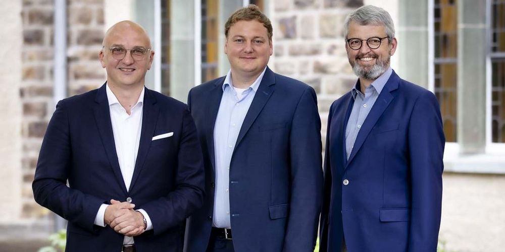 Gruppenbild von drei Männern in Anzügen, die in die Kamera lächeln
