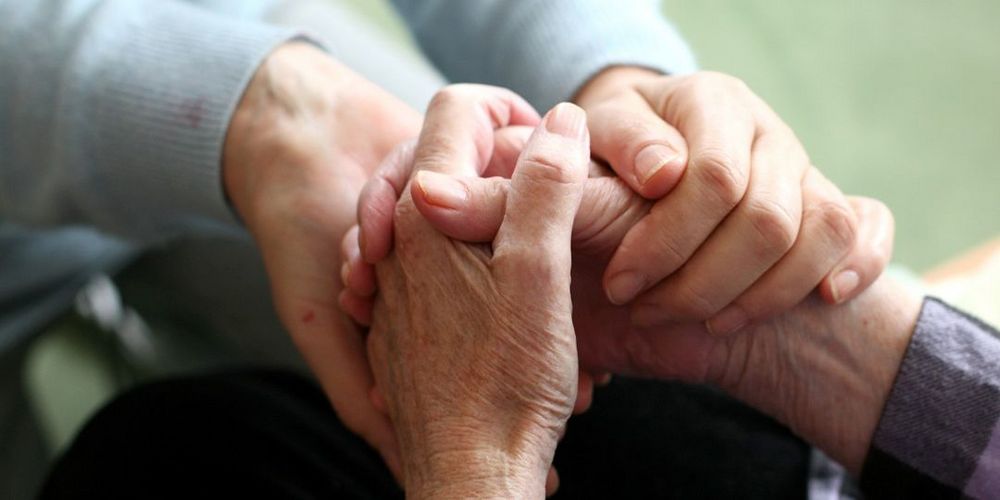 Seelische und körperbezogene Unterstützung in der ambulanten Pflege Eine Pflegefachkraft hält die Hände einer Bewohnerin in der ambulanten Pflege.
