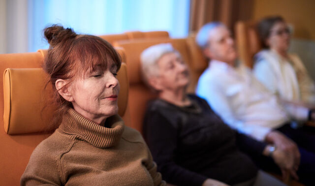 Das Bild zeigt vier ältere Menschen, die mit geschlossenen Augen nebeneinander sitzen.