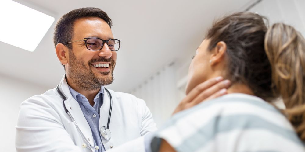 Welche Symptome treten bei einer Schilddrüsenvergrößerung auf? Ein Arzt untersucht eine Patientin mit Symptomen einer Schilddrüsenvergrößerung.