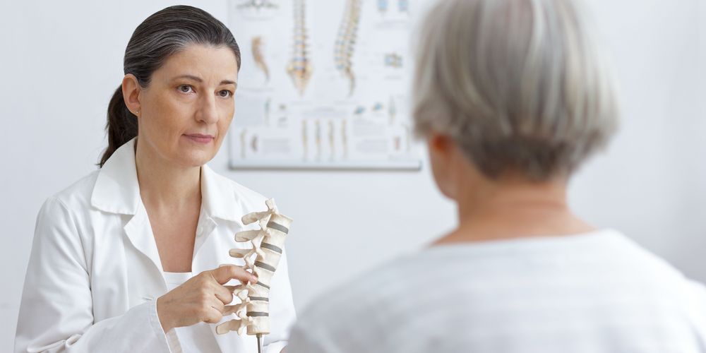 Osteoporose erkennen Eine Ärztin erklärt einer Patientin mit Hilfe eines Wirbelsäulenmodells, was eine Osteoporose ist.