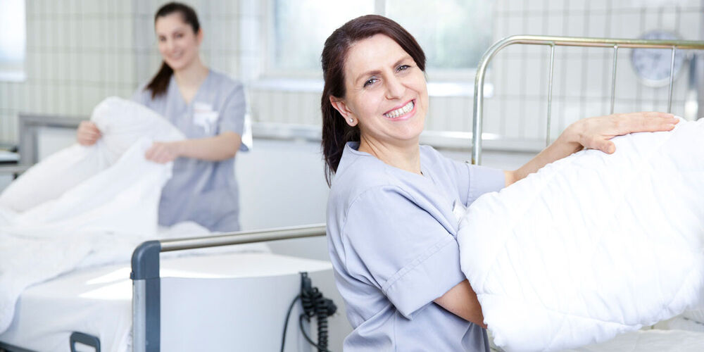 Zwei Mitarbeiterinnen richten Patientenbetten her und beziehen diese neu. 