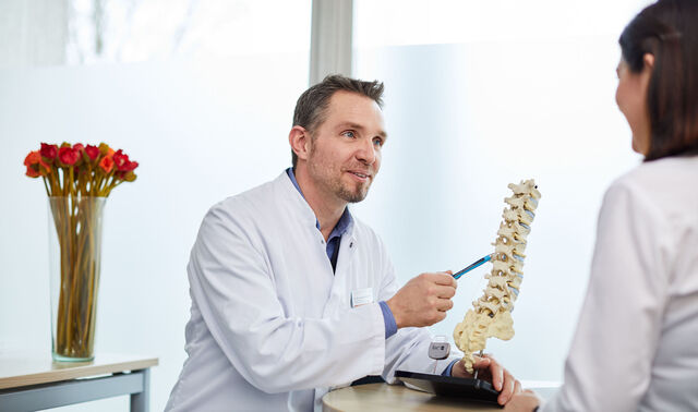 Ein Arzt aus dem Fachbereich Wirbelsäulentherapie erklärt einer Patientin den Behandlungsablauf.
