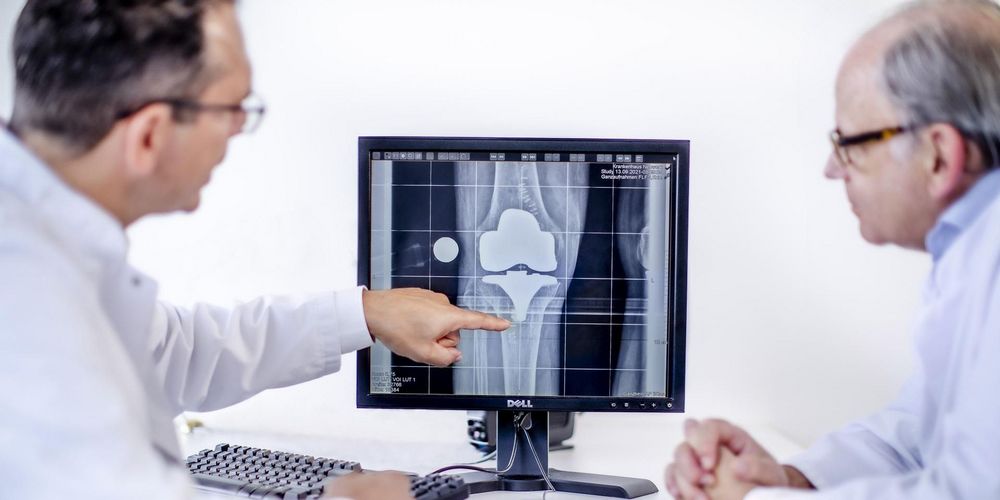 Ein Orthopäde erklärt einem Patienten der orthopädischen Ambulanz die Behandlung des Kniegelenks.