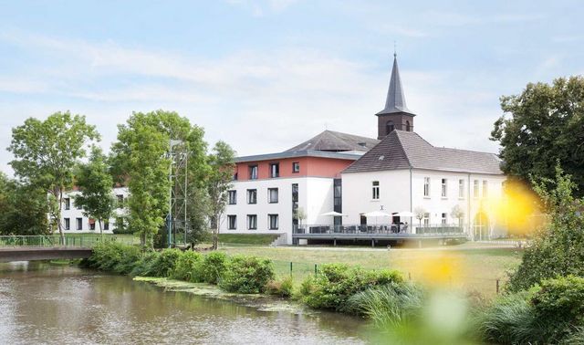 Außenansicht des Haus Maria Hilf. Vor diesem ist ein Fluss mit einer Brücke.