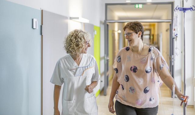 Eine Mitarbeiterin der lokalen Tumortherapie ist mit einer Patientin unterwegs in der Klinik.