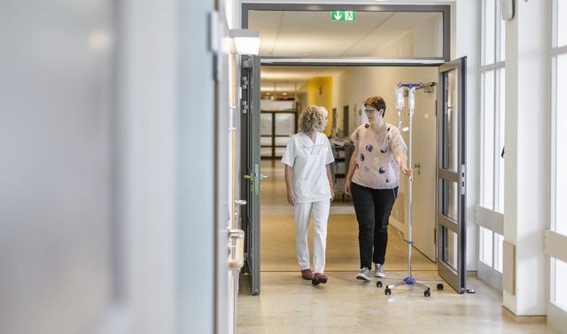 Eine Mitarbeiterin begleitet eine Patientin der onkologischen Chirurgie auf dem Flur einer Klinik.