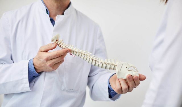 Ein Arzt für Wirbelsäulenchirurgie erklärt einem Patienten eine Deformität am Wirbelsäulen-Modell.
