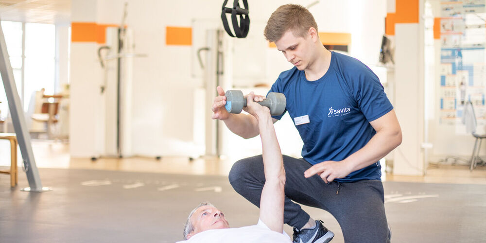 Ein Mitglied des therapeutischen Teams führt innerhalb der orthopädischen Reha Übungen mit einem Patienten aus.