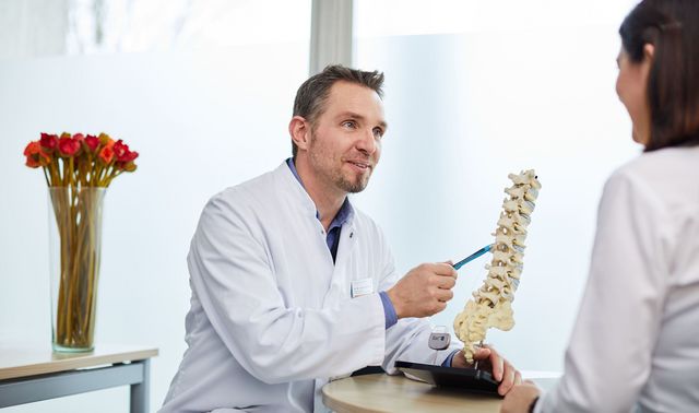 Was bedeutet Wirbelsäulentherapie? Ein Arzt erklärt einer Patientin, wie die Wirbelsäulentherapie funktioniert.