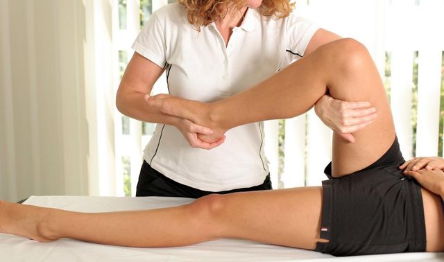 Eine Therapeutin führt bei der Physiotherapie Übungen mit dem Bein durch.